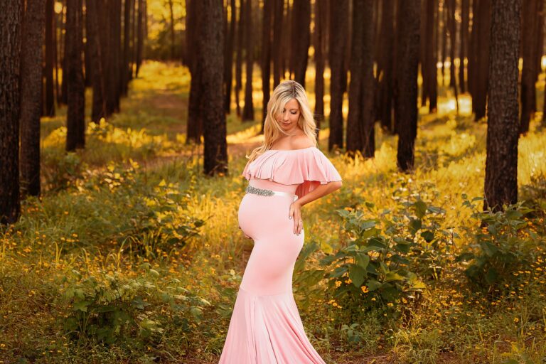 pregnant woman in pink maternity gown with silver belt in a golden forest looking at her bump Houston Doulas