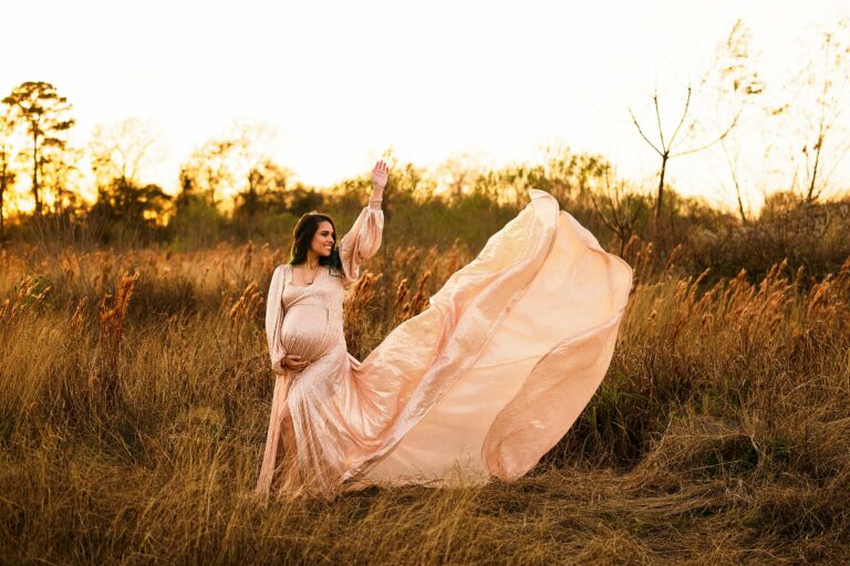 mom to be in a peach maternity gown in a field with her train flying houston midwives