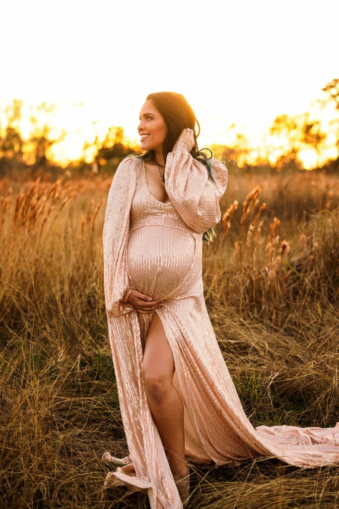 pregnant woman in peach maternity gown standing in a field at sunset houston midwives