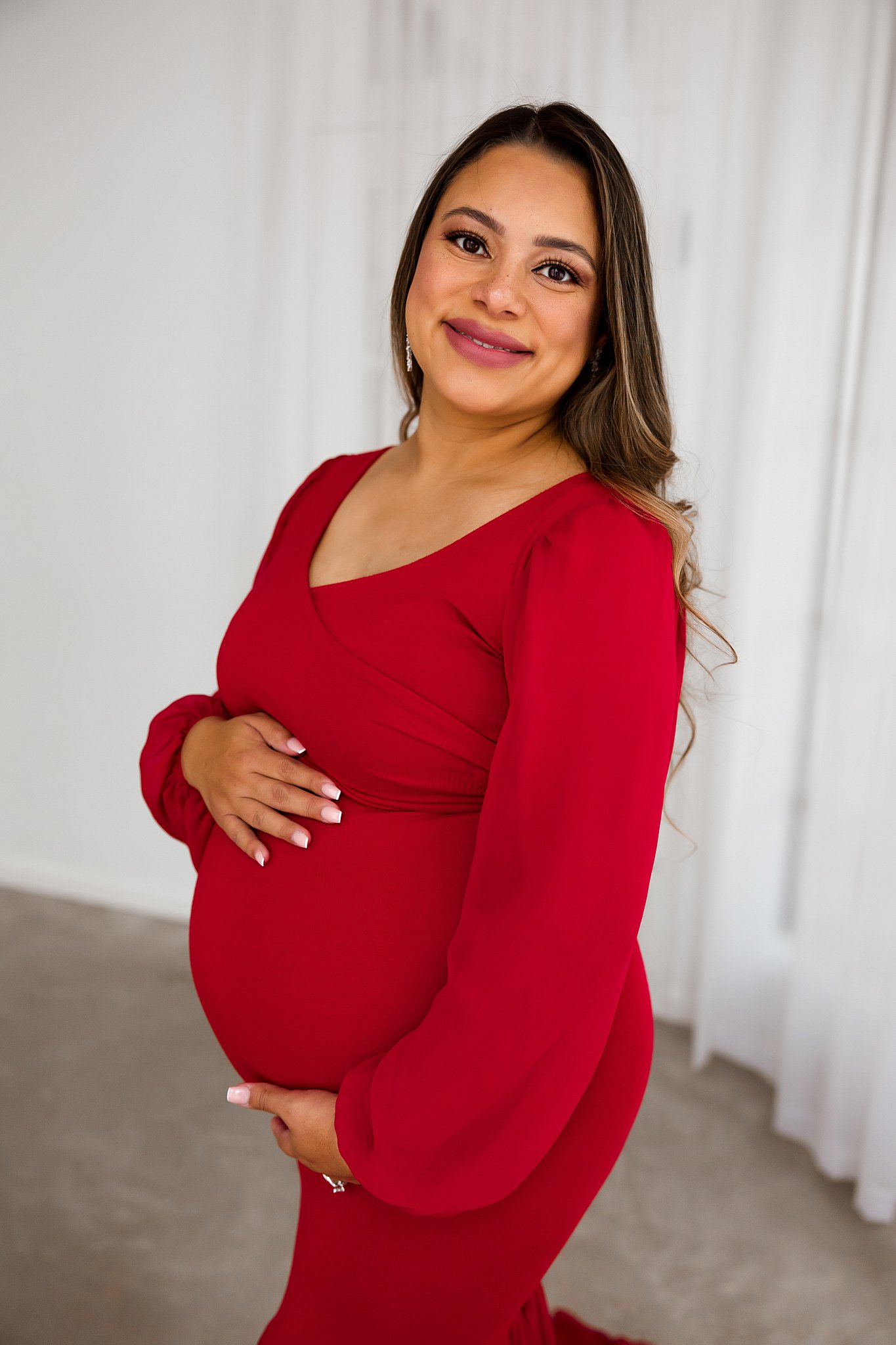 mom to be stands in a red maternity gown holds the top and bottom of her bump houston birth center